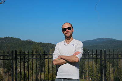 Scott Demeules with his arms crossed and sunglasses on with blue skies and grassy hills in the background.